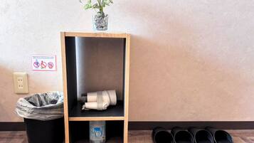 Una estantería de madera con una planta en maceta, un bote de basura y un par de pantuflas negras.