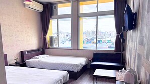 A hotel room with two beds, a desk, a TV, and a view of the city. - My Place - Hostel (Naha)