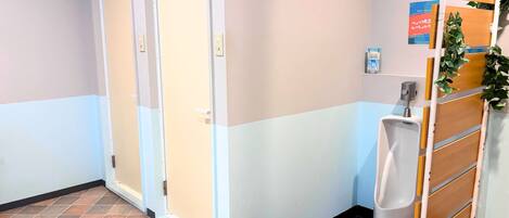 A hotel hallway with a tiled floor, a urinal, a trash bin, and a door.