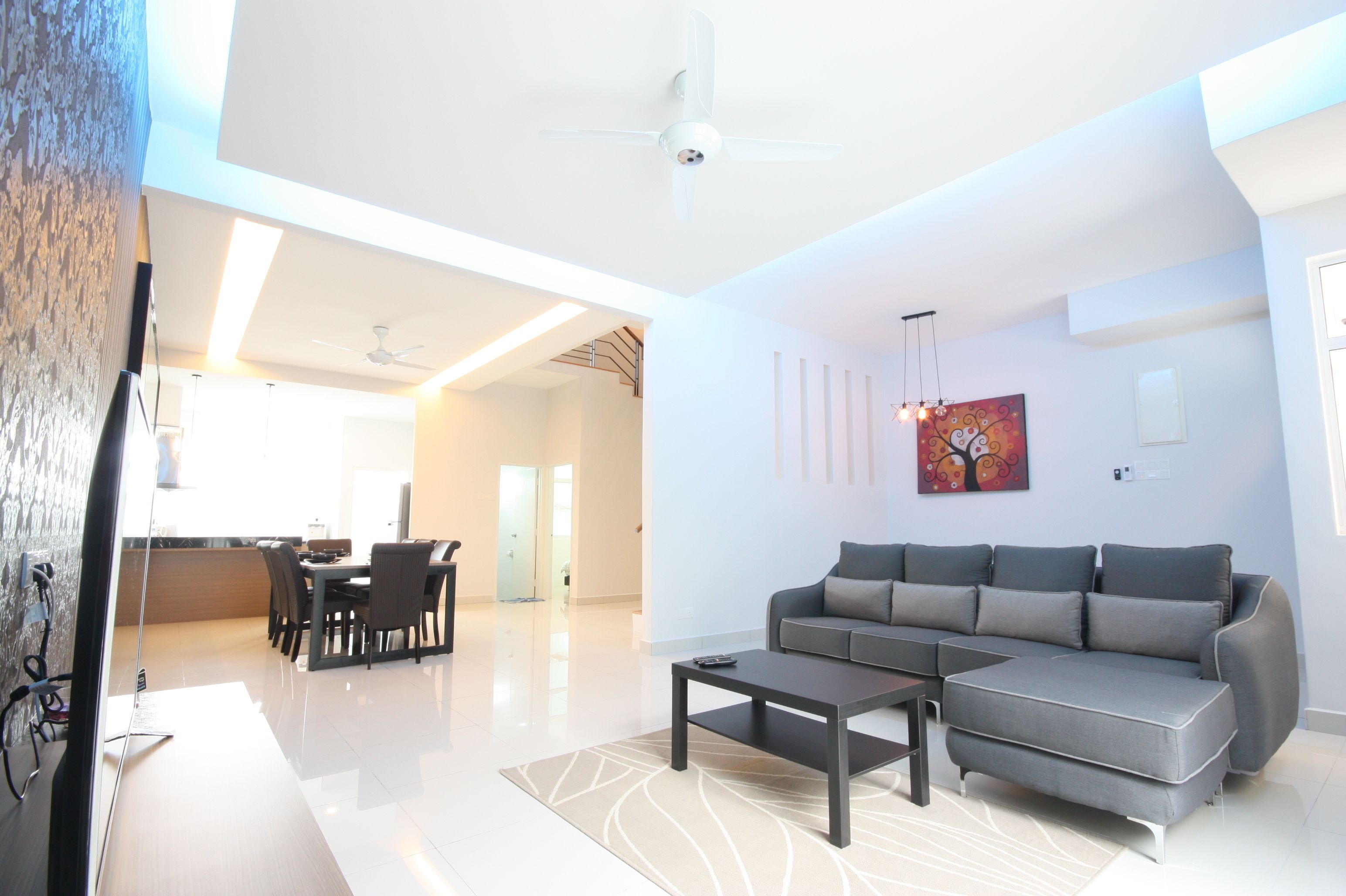 Una sala de estar moderna con un sofá seccional gris, una mesa de centro y una zona de comedor con sillas y una mesa.