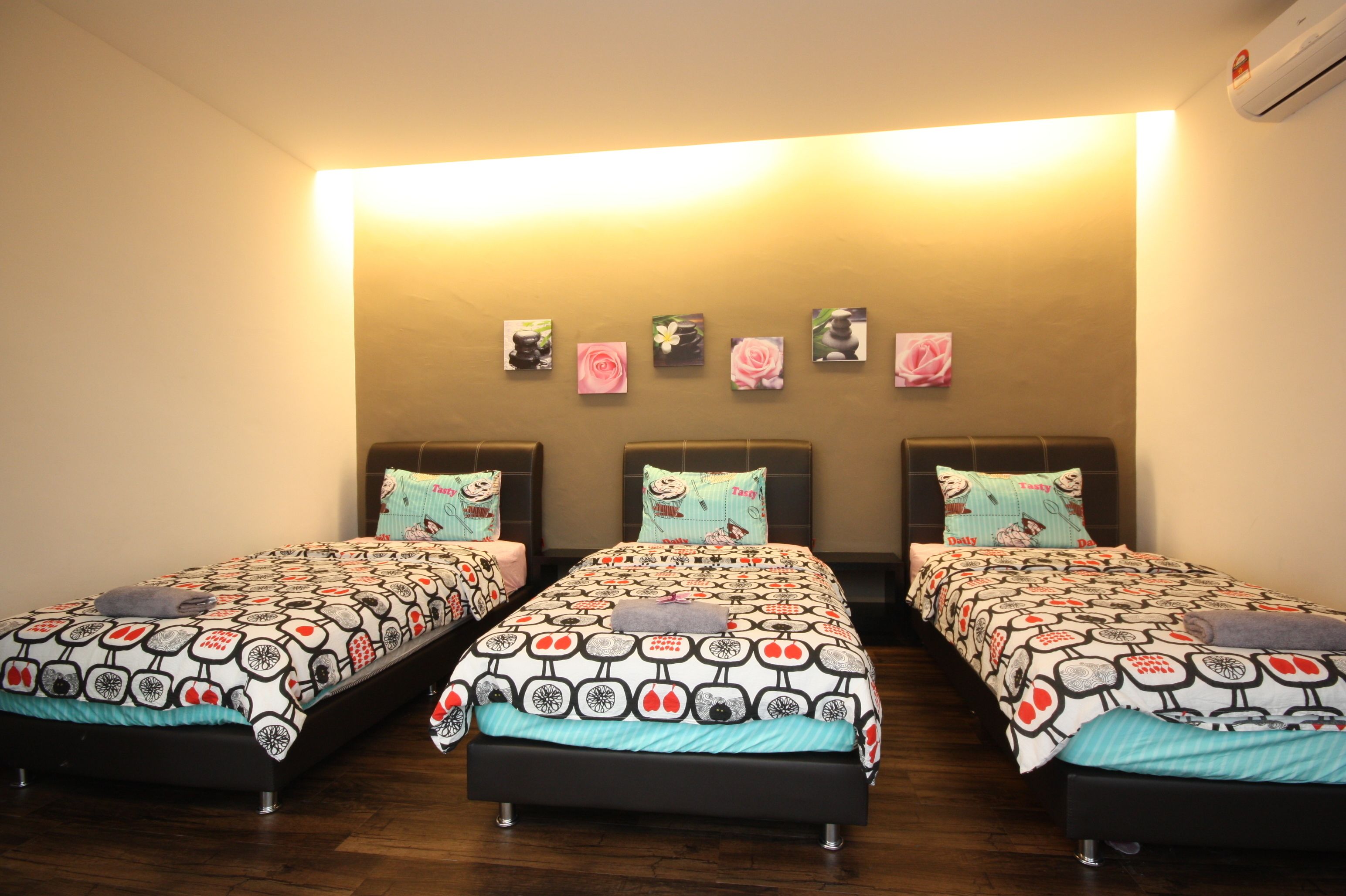 Een hotelkamer met drie enkele bedden, elk met een bedovertrek met dessin en passende kussens. De kamer heeft een houten vloer en een grote wandlamp.