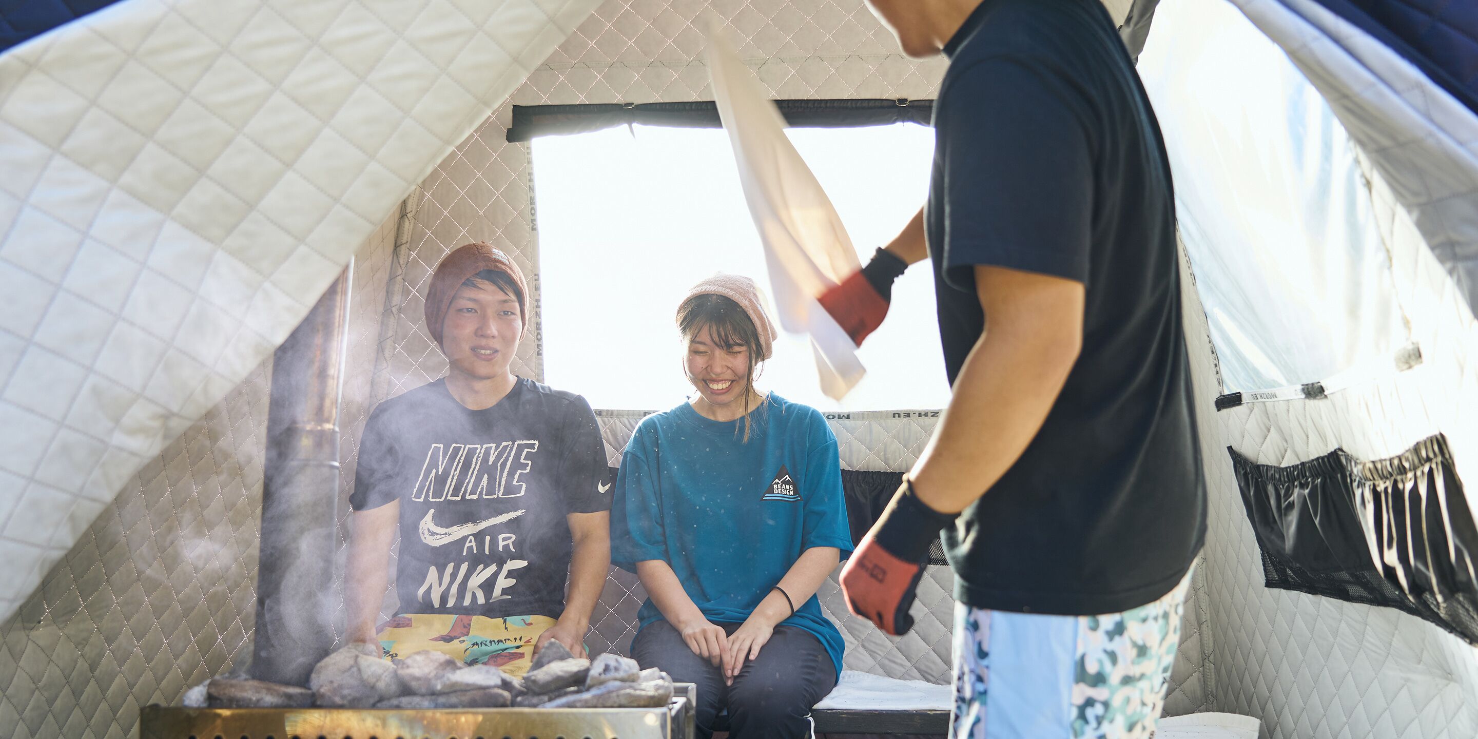A tent with a quilted interior, a grill with food, and people sitting inside.