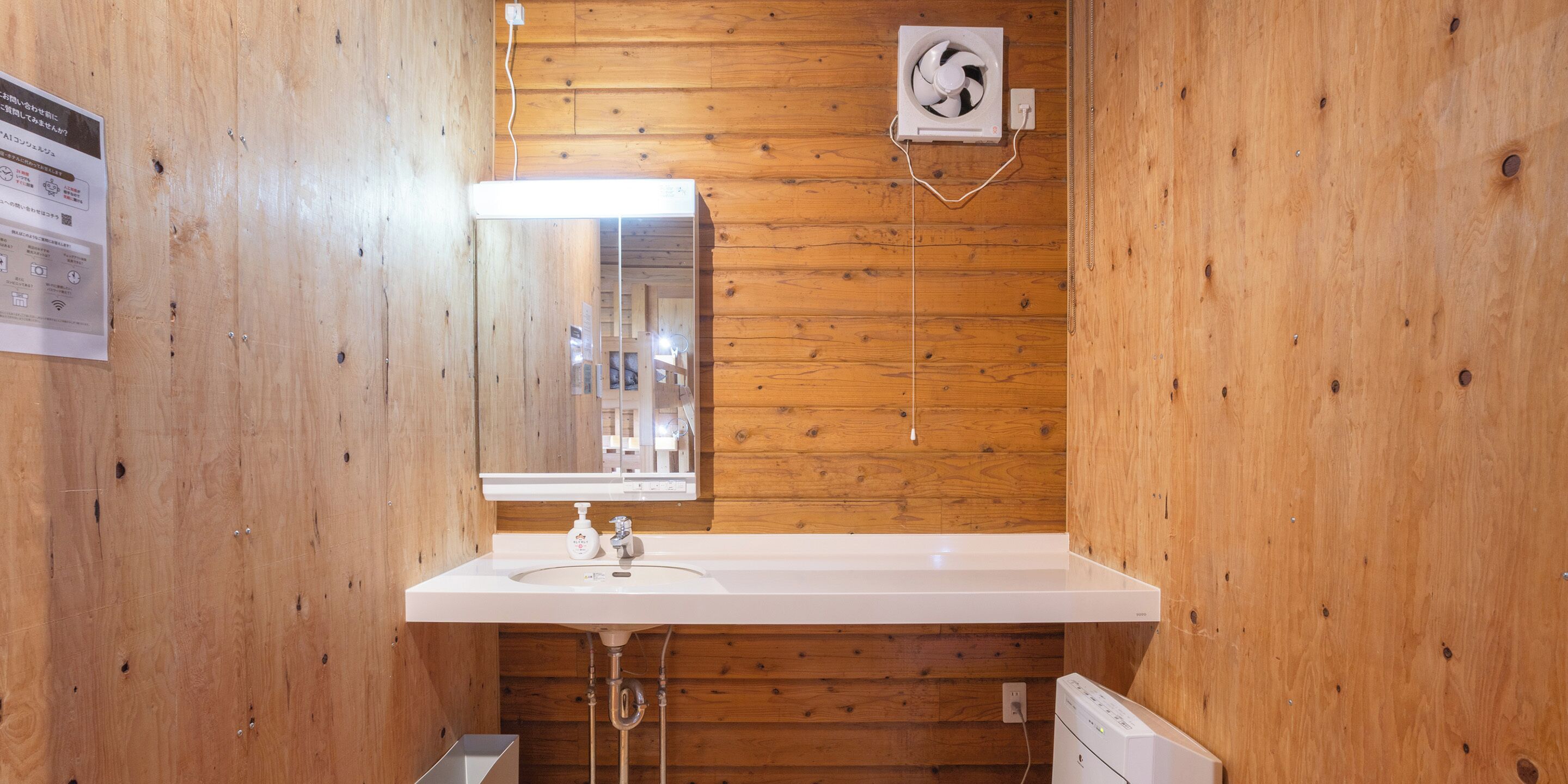 A wooden-paneled bathroom with a white sink, mirror, and a wall-mounted fan.