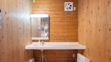 A wooden-paneled bathroom with a white sink, mirror, and a wall-mounted fan.