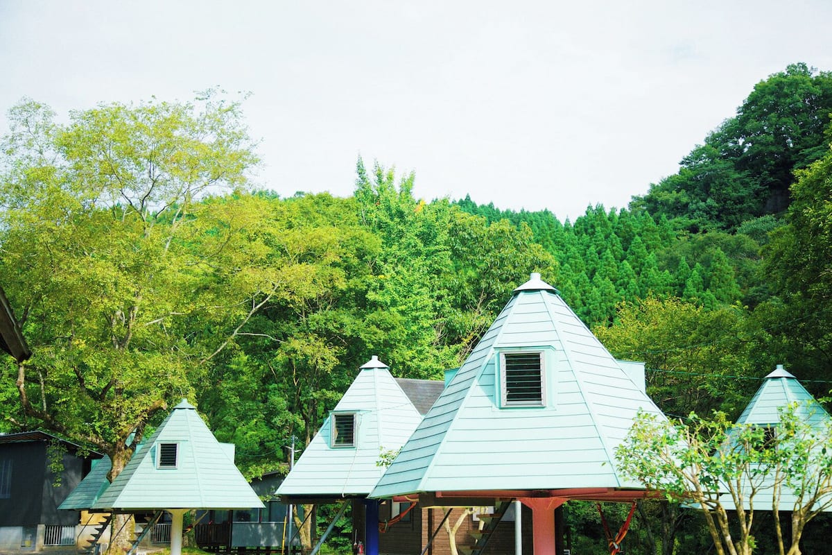 Une rangée de petites cabanes aux toits bleu clair, avec une forêt en arrière-plan.