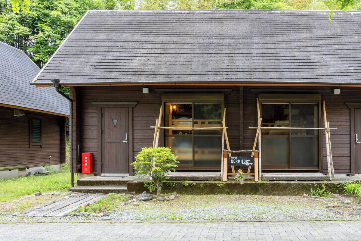 Une cabane en bois dotée d’une grande fenêtre et d’une porte, entourée de verdure.
