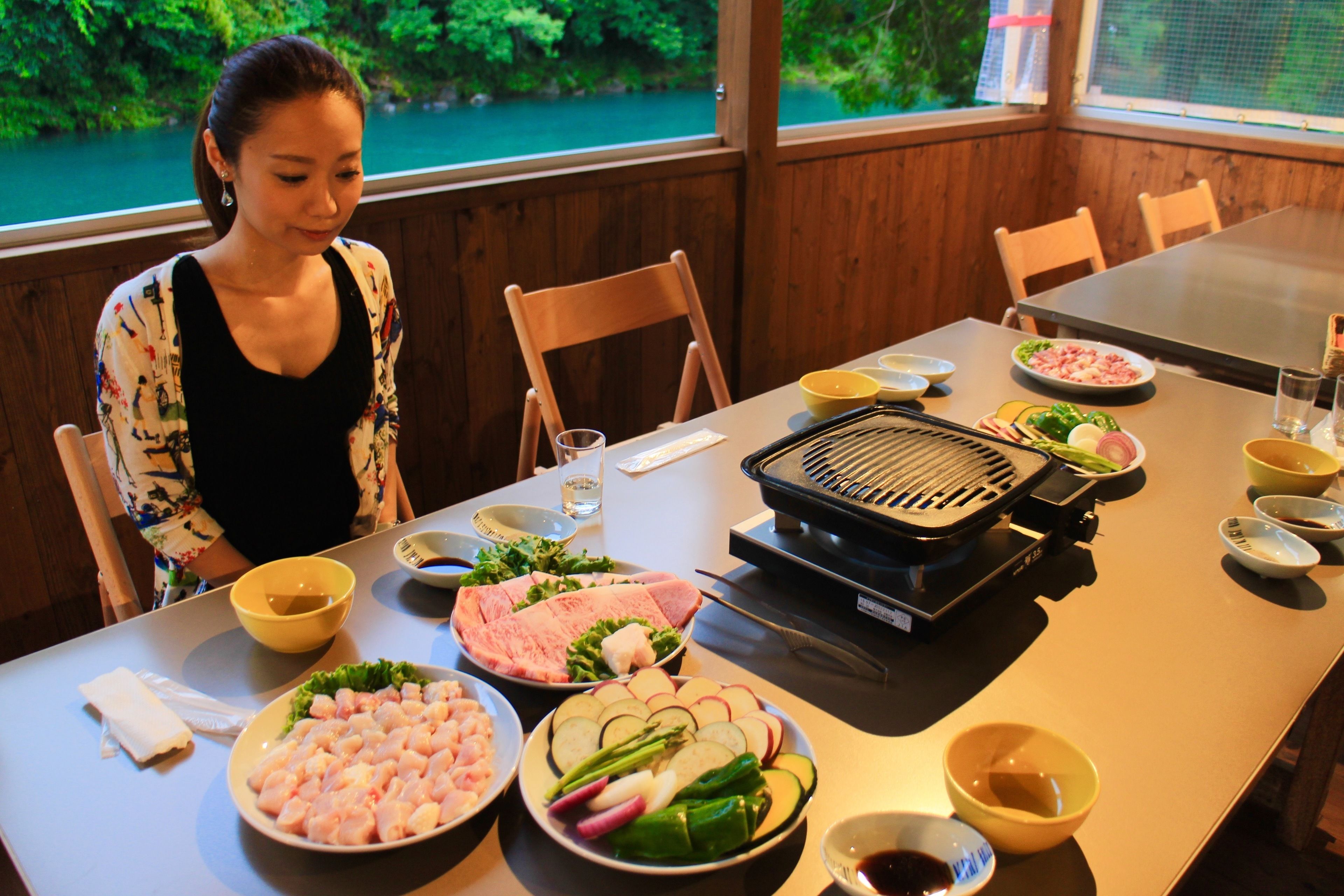 A dining table with various food items and a grill, set in a room with wooden walls and a view of greenery outside.
