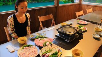 A dining table with various food items and a grill, set in a room with wooden walls and a view of greenery outside.