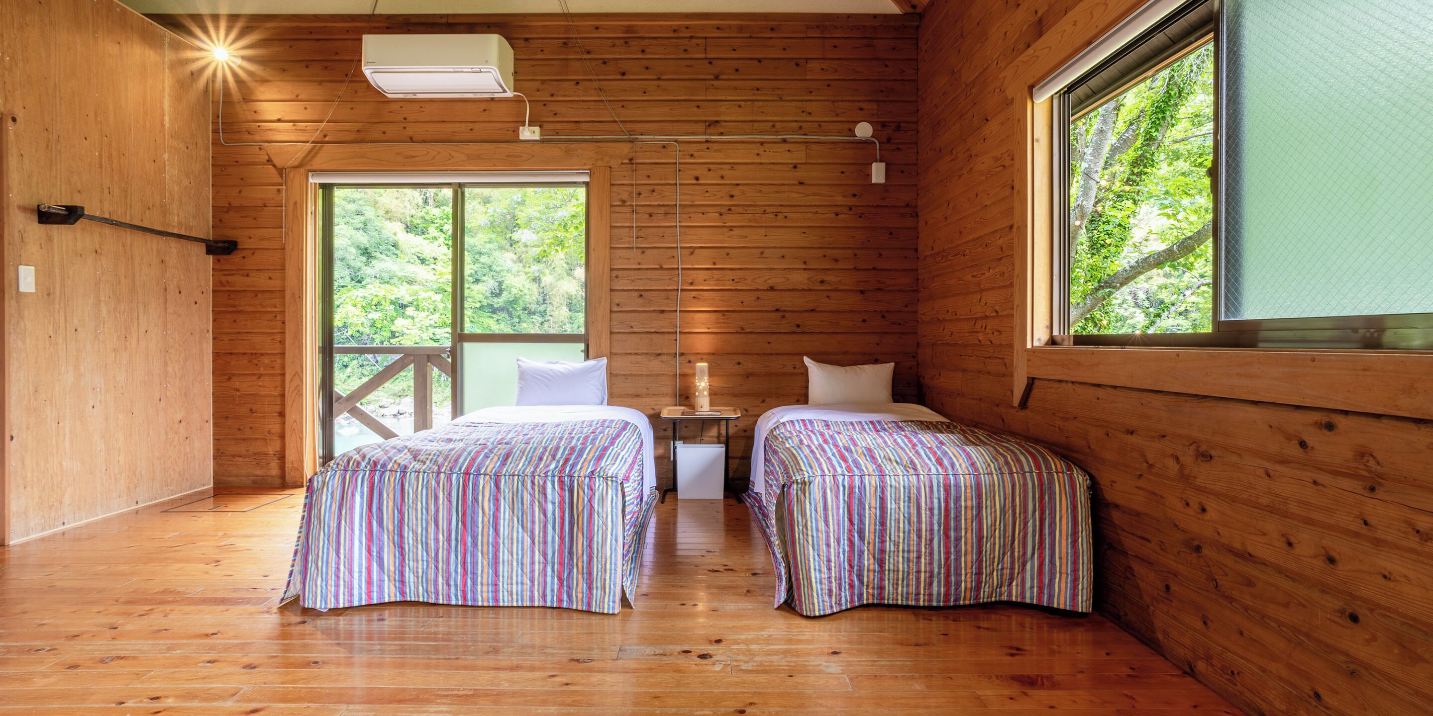 A wooden cabin room with two beds, a window, and a nightstand.