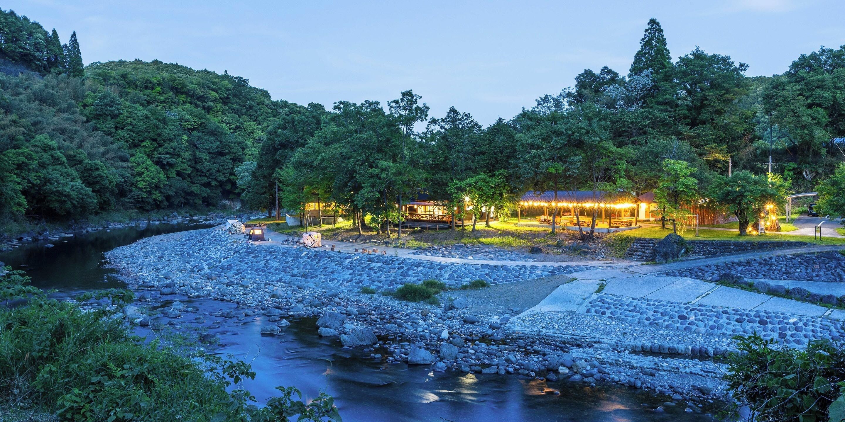 A riverside hotel with a stone pathway leading to the entrance, surrounded by lush greenery and trees.
