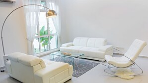 A modern living room with a white sofa, a white armchair, a glass coffee table, and a floor lamp. - Shamrock Beach Villas 12 (George Town)