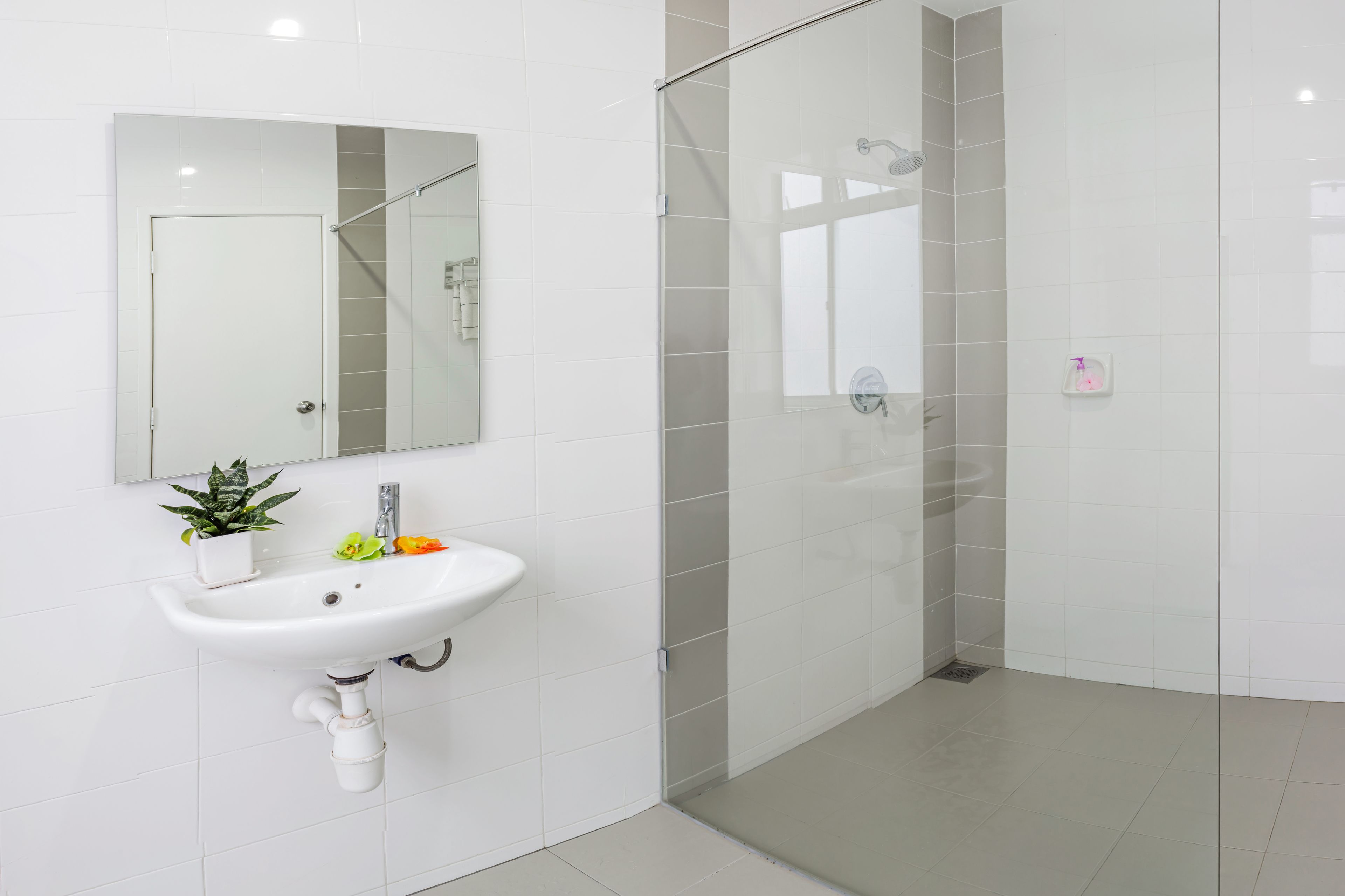 A modern bathroom with a white sink, mirror, and glass shower enclosure.