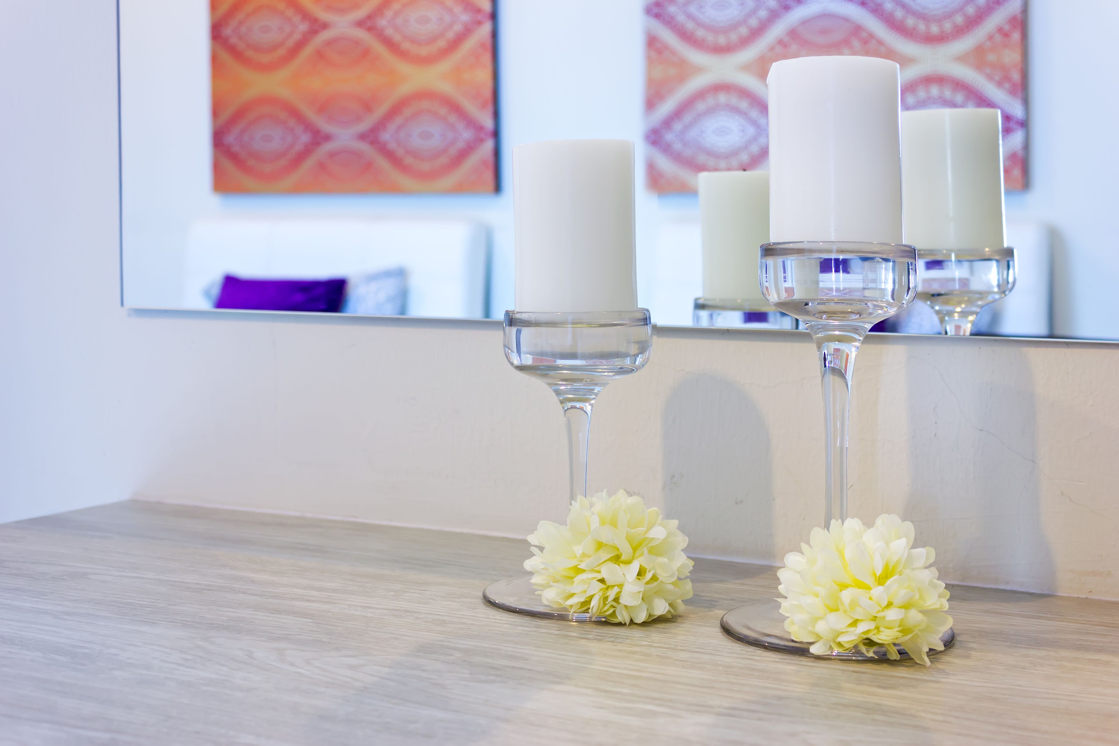 A bathroom with a mirror, two candles in glass holders, and two artificial flowers on the counter.