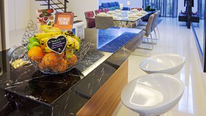 A modern hotel lobby with a marble reception desk, a fruit basket, a sign for George Town, and a dining area in the background. - Shamrock Beach Villas 12 (George Town)