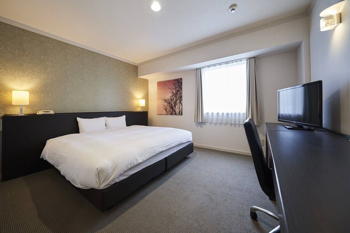 A hotel room with a bed, a desk, a television, and a window with curtains.