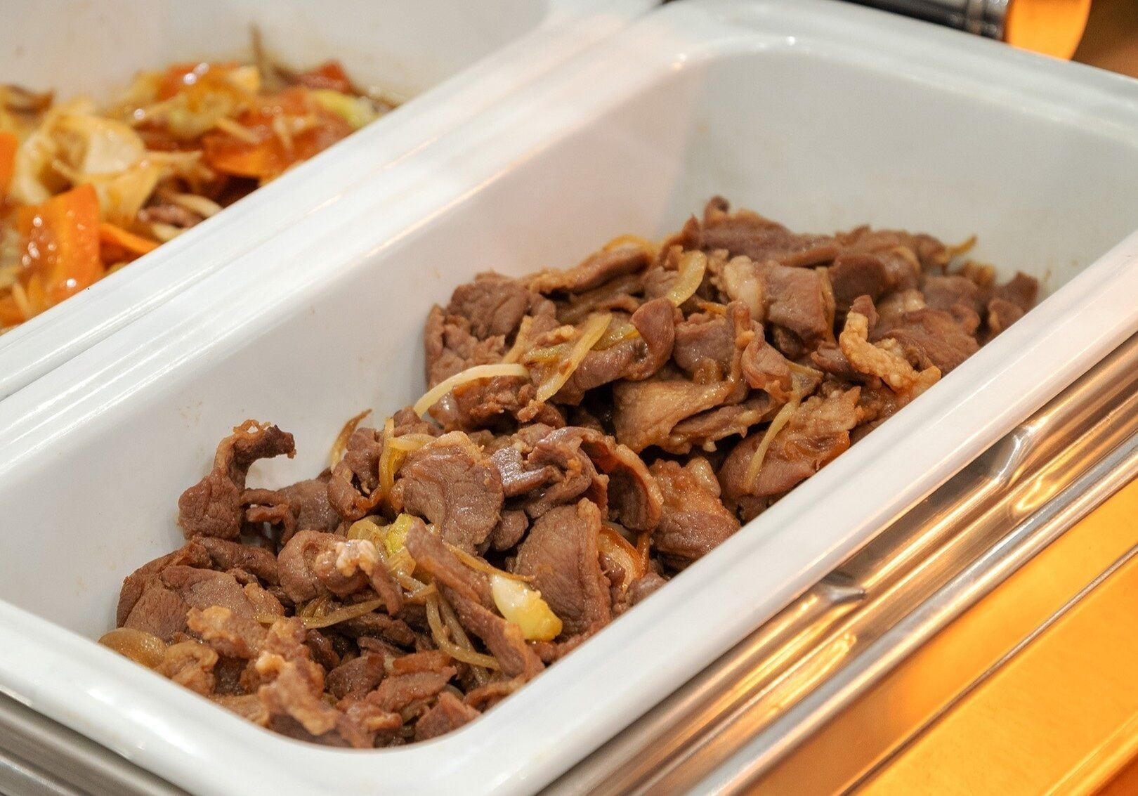 A white rectangular serving dish filled with cooked beef and onions.