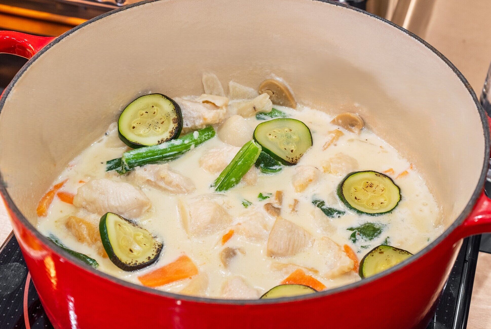 A red pot filled with a creamy soup containing vegetables and chunks of meat.