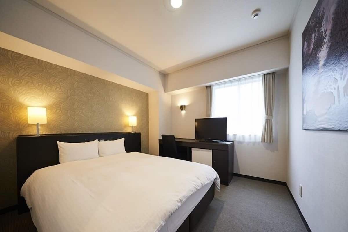 A hotel room with a large bed, a desk with a television, and a window with curtains.