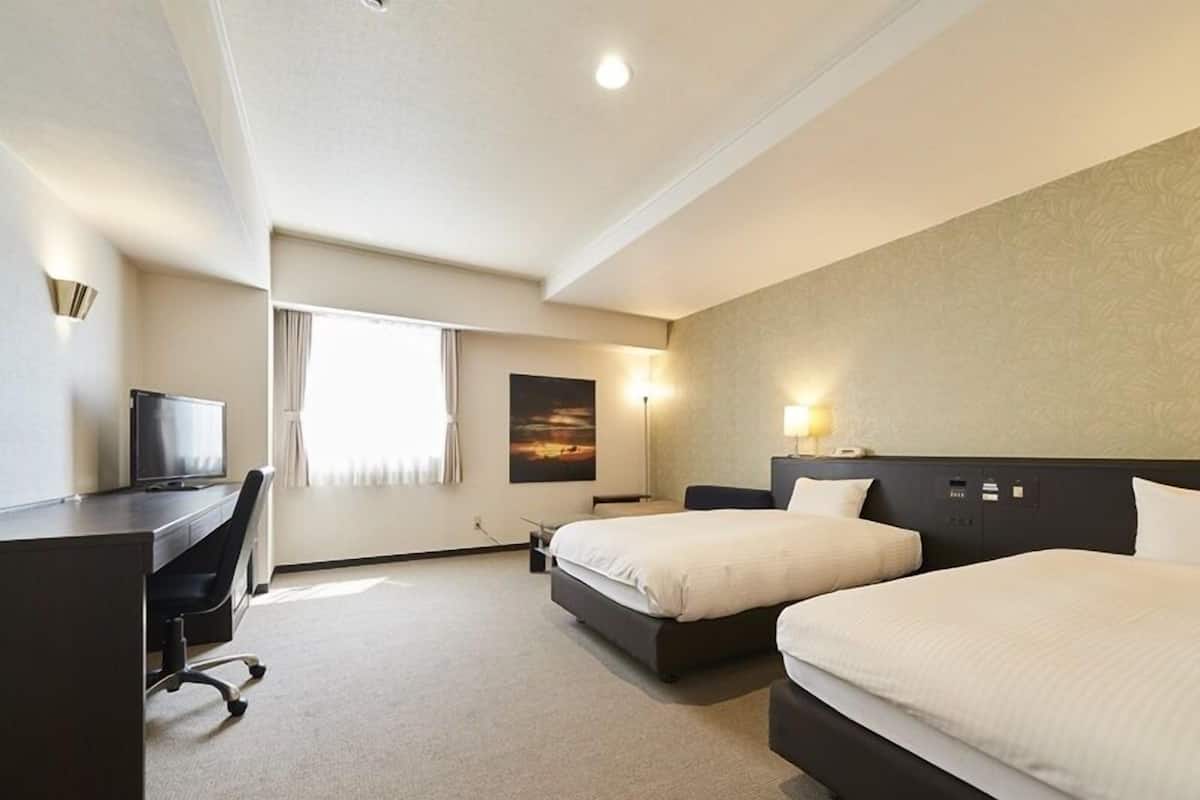 A hotel room with two beds, a desk with a chair, a television, and a painting on the wall.