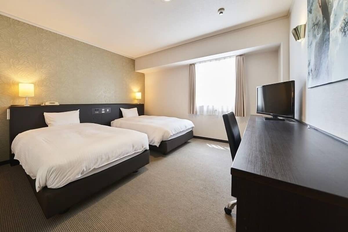 A hotel room with two beds, a desk, a TV, and a large window.