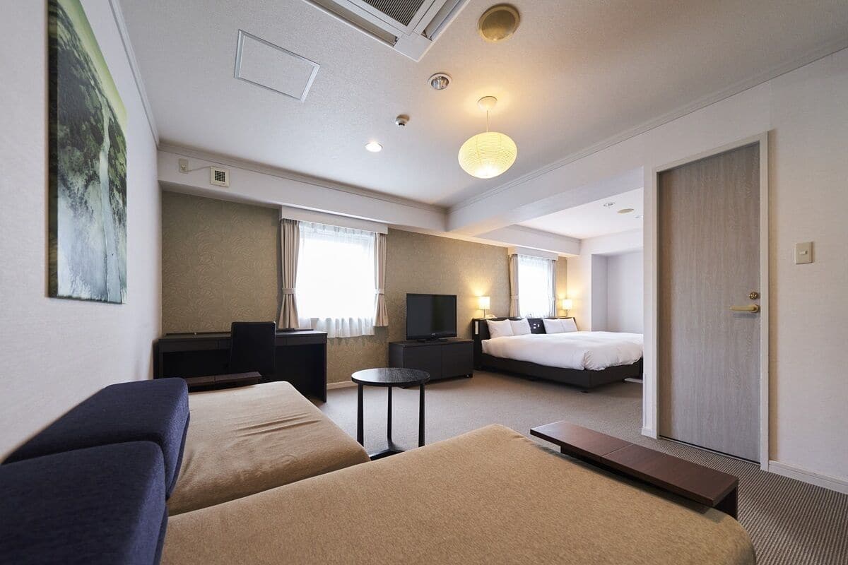 A hotel room with two beds, a TV, a desk, and a sofa.