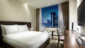 Habitación de hotel con una cama grande, un escritorio con silla, una mesita con una planta y un televisor en la pared.