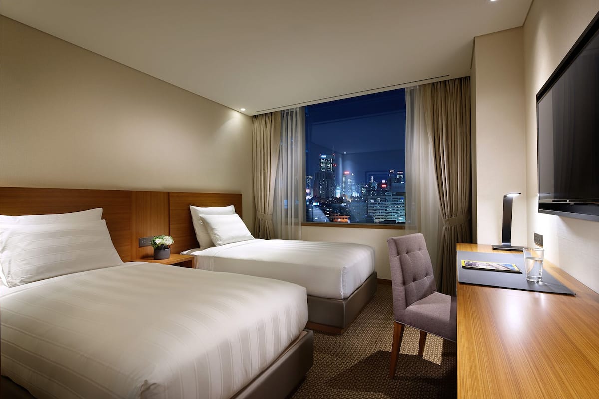 A hotel room with two beds, a desk, a chair, a TV, and a city view.