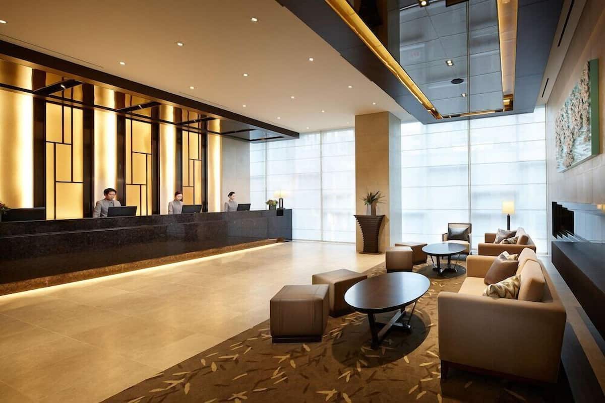 A modern hotel lobby with a reception desk, seating area, and large windows.