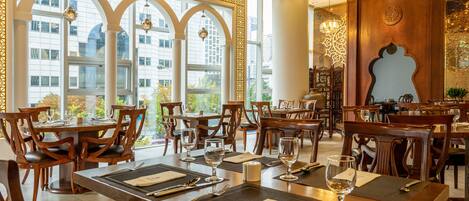 Een restaurant met houten tafels en stoelen, grote ramen en decoratieve verlichting.