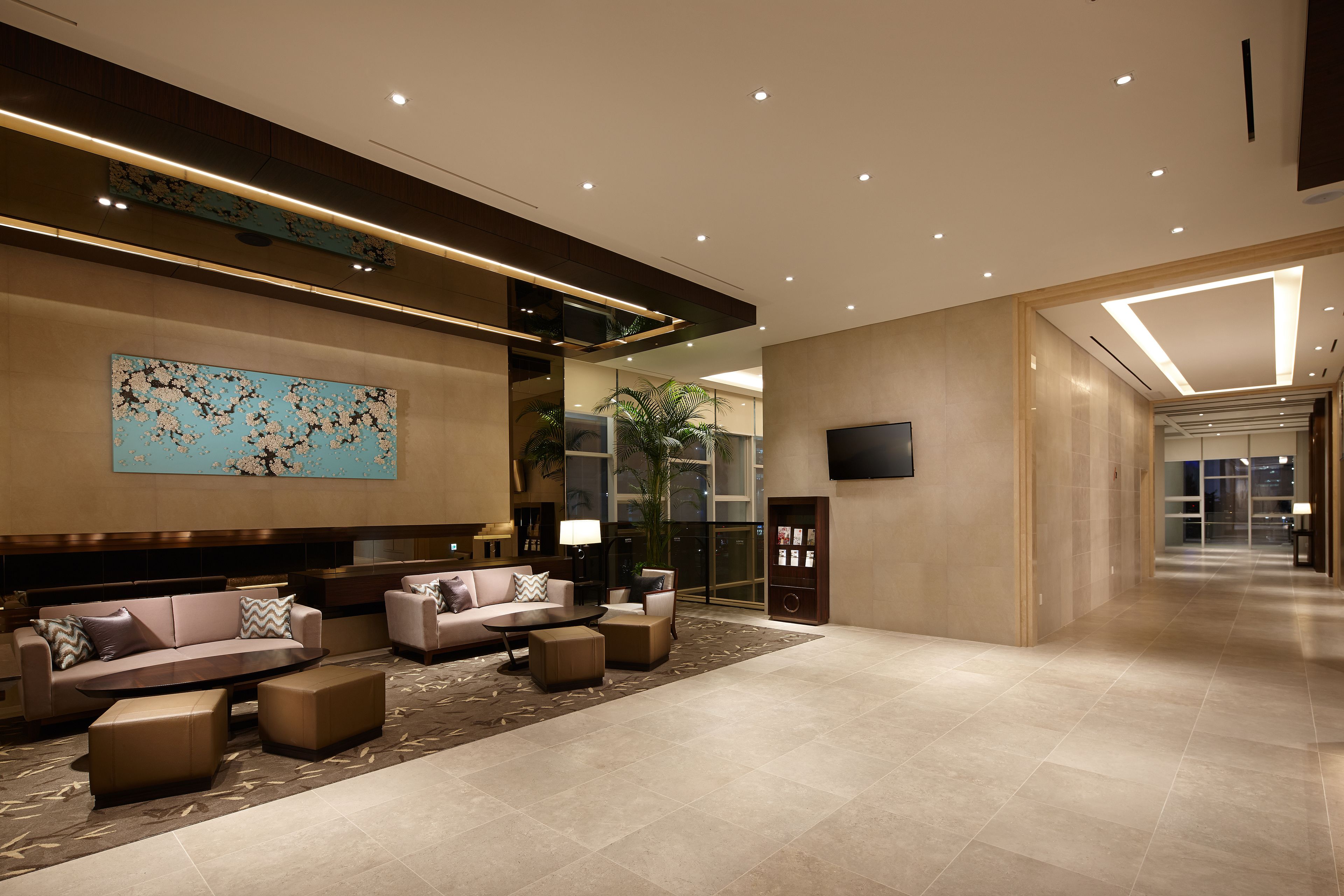 A spacious lobby with a modern design, featuring a large seating area with sofas and ottomans, a large abstract painting on the wall, and a flat-screen TV mounted on the wall.