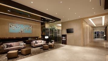 Un hall d’entrée spacieux au design moderne, comprenant un grand espace salon avec des canapés et des poufs, une grande peinture abstraite au mur et un téléviseur à écran plat fixé au mur.