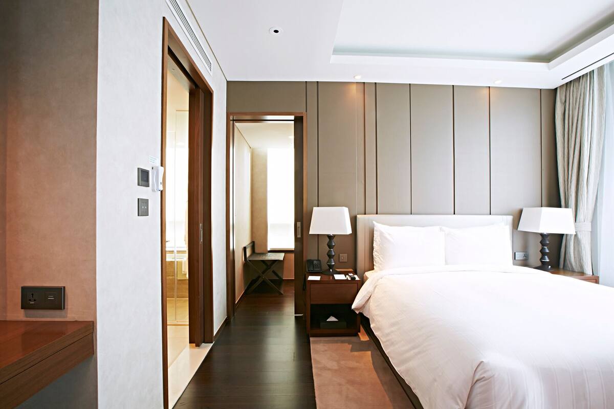A hotel room with a large bed, bedside lamps, a nightstand, a wooden desk, and a view of the hallway.