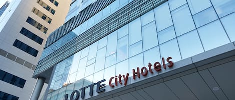 Una entrada de hotel moderna con fachada de vidrio y un letrero que dice "LOTTE City Hotels".