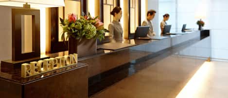 Un mostrador de recepción con una lámpara, una planta en maceta y un letrero que dice "RECEPTION".
