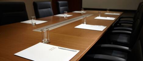 Un salón de conferencias con una larga mesa, sillas negras y una pantalla de proyector.