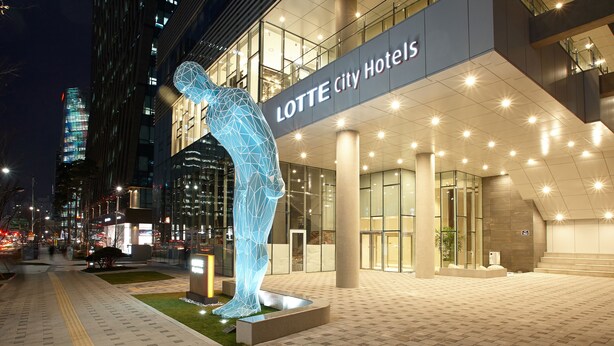 A modern hotel entrance with a prominent geometric sculpture, a well-lit facade, and a cityscape in the background. - LOTTE CITY HOTEL MYEONGDONG (Seoul)