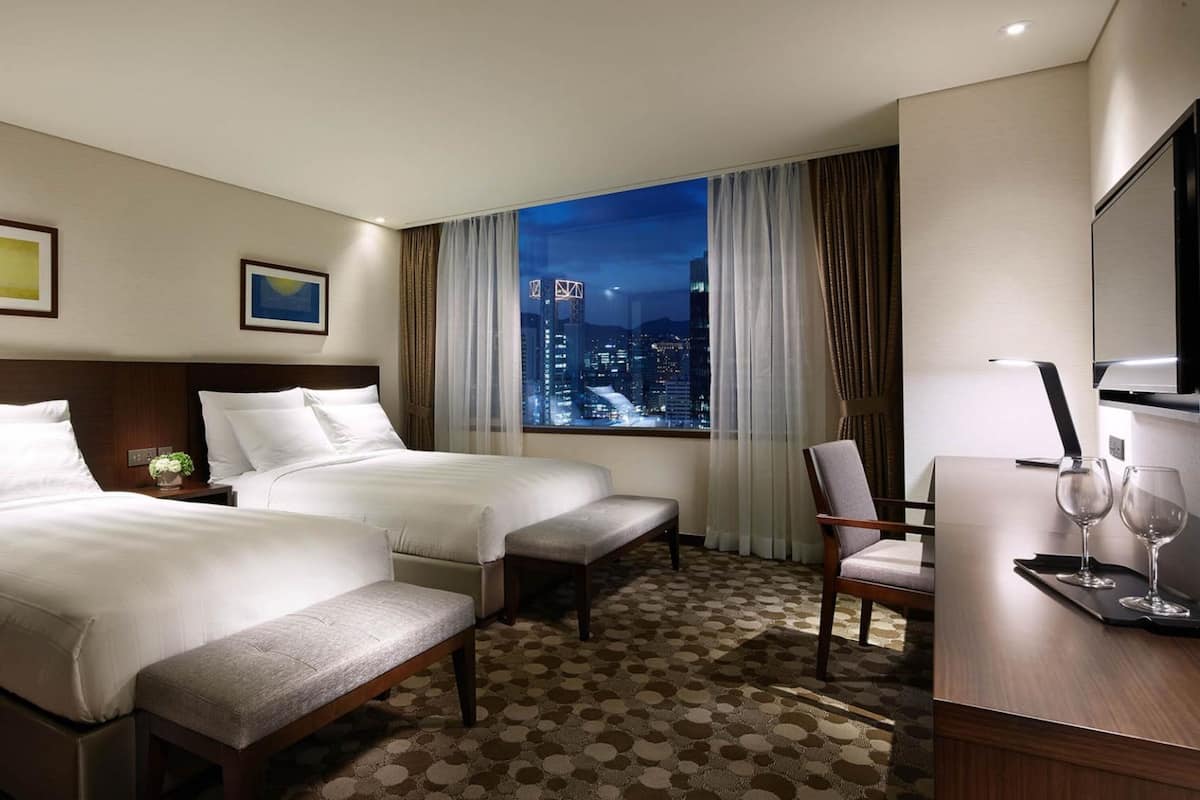 A hotel room with two beds, a desk with a chair, a TV, and a city view.