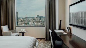 A hotel room with a large window offering a city view, a bed, a desk, and a chair. - LOTTE CITY HOTEL MYEONGDONG (Seoul)