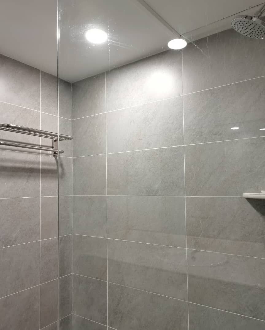 A modern shower area with grey tiles, a metal towel rack, and a ceiling-mounted showerhead.