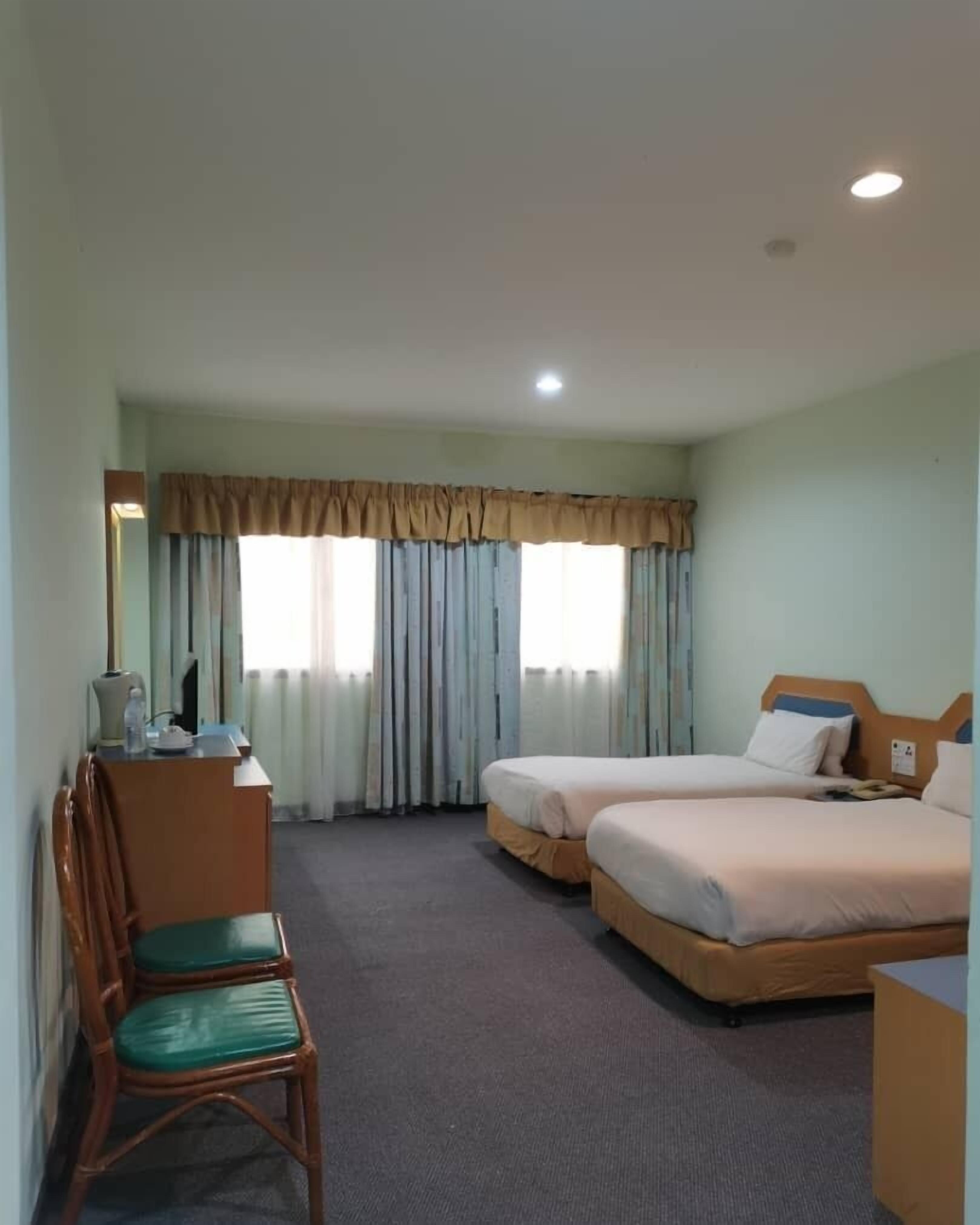Habitación de hotel con dos camas, un escritorio con silla y una ventana con cortinas.