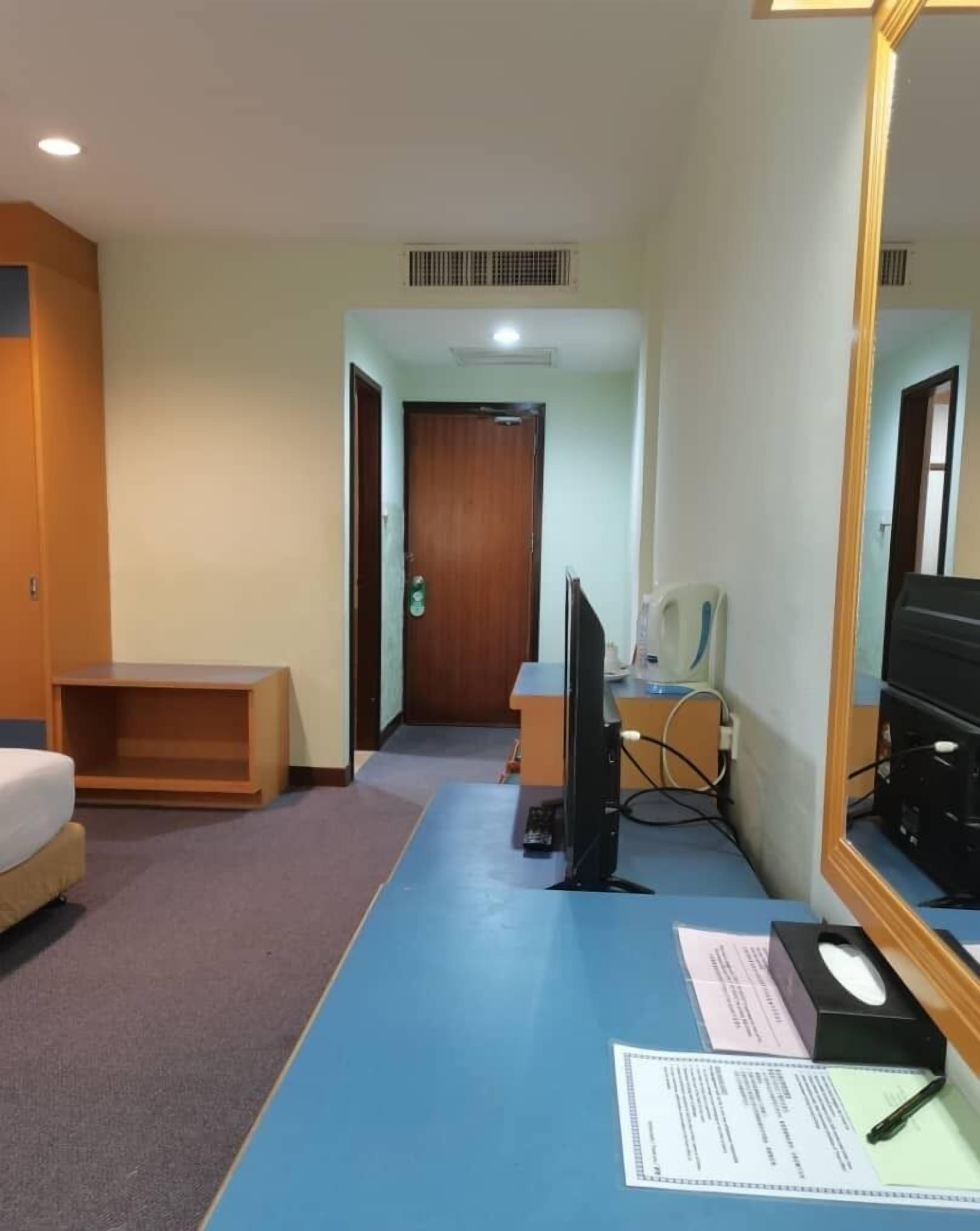 A hotel room with a bed, a desk with a computer, a chair, and a mirror.