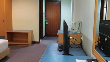 A hotel room with a bed, a desk with a computer, a chair, and a mirror.