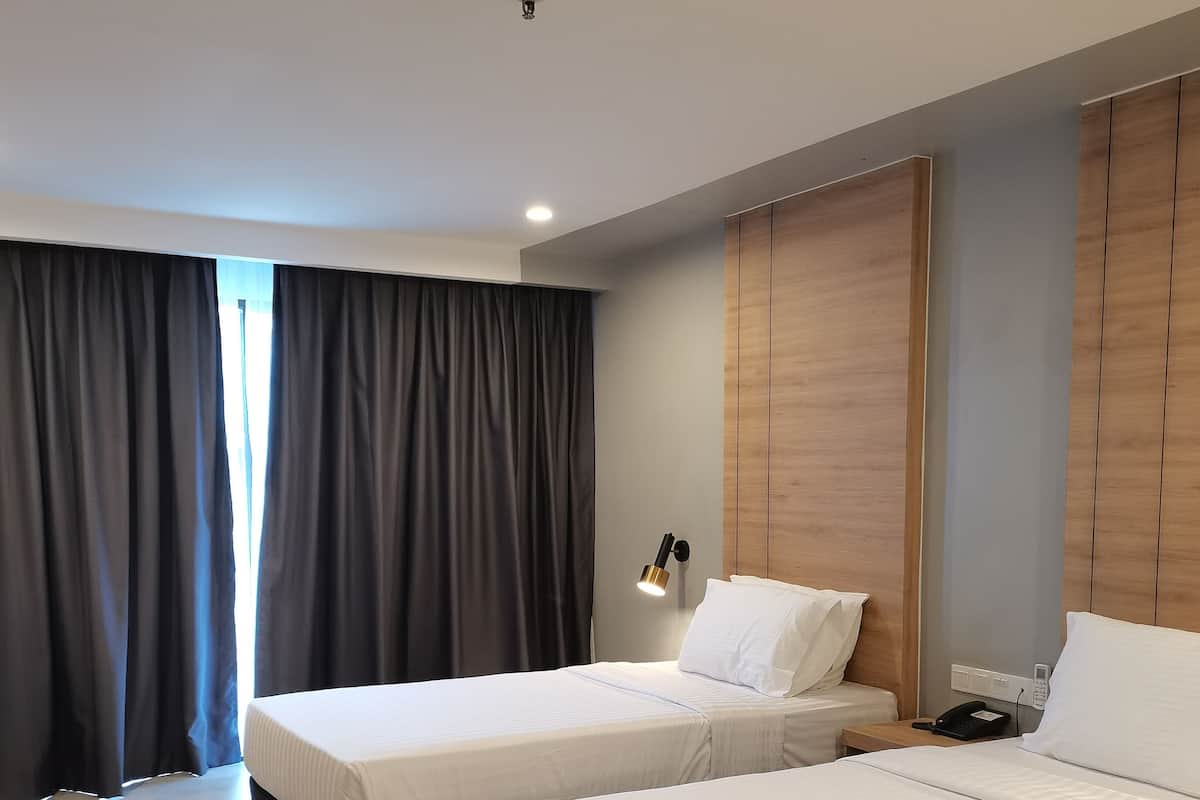 Una habitación de hotel moderna con dos camas, una mesita de noche con lámpara y un ventanal con cortinas.