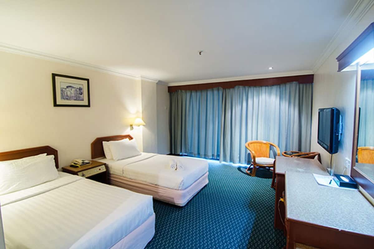 Una habitación de hotel con dos camas, un escritorio con silla, televisión y ventana con cortinas.