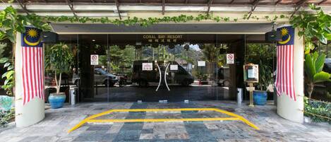 The entrance to Coral Bay Resort with a covered walkway, Malaysian and American flags, and a sign indicating no parking.