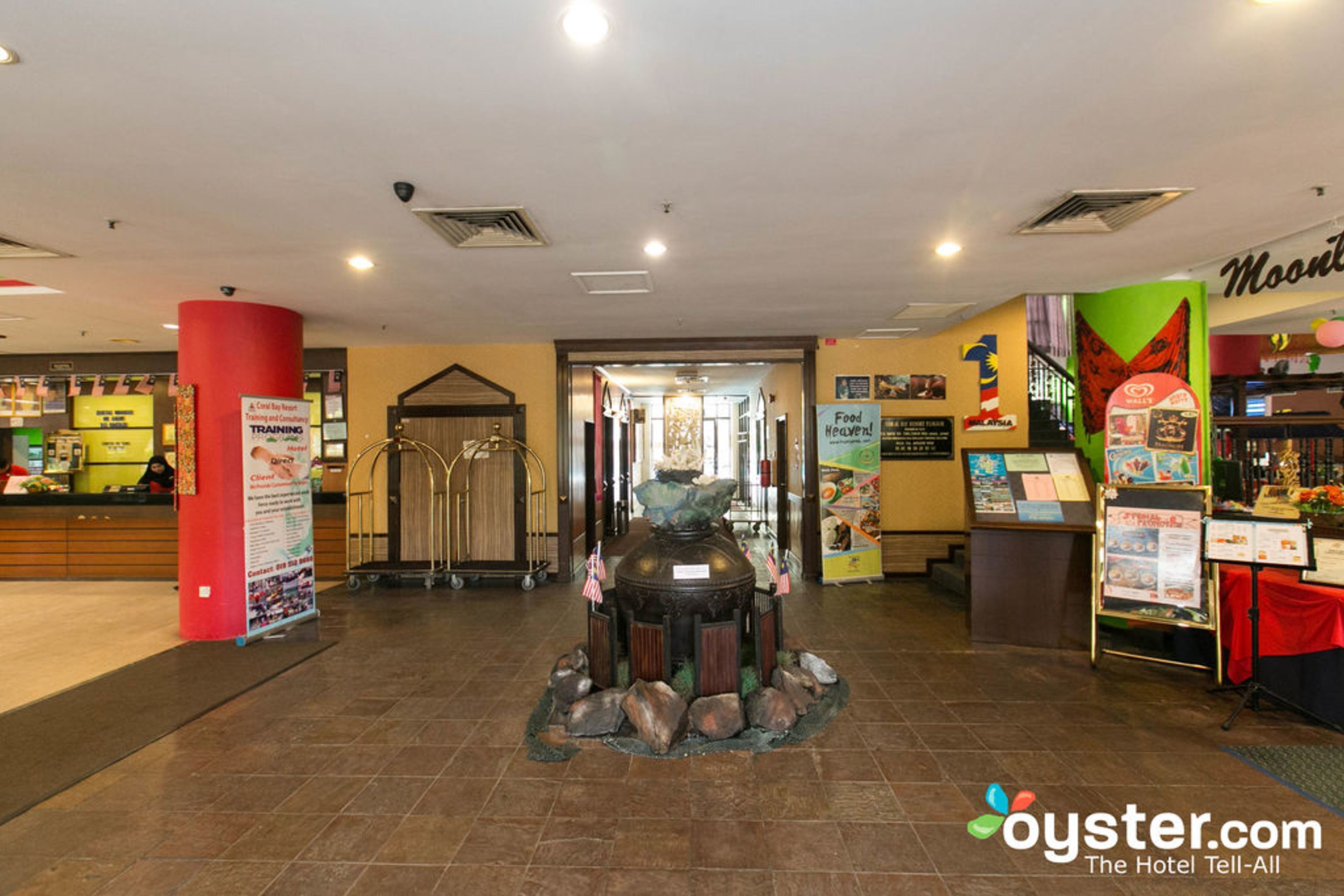 A hotel lobby with a reception desk, a decorative fountain, and a food court area.