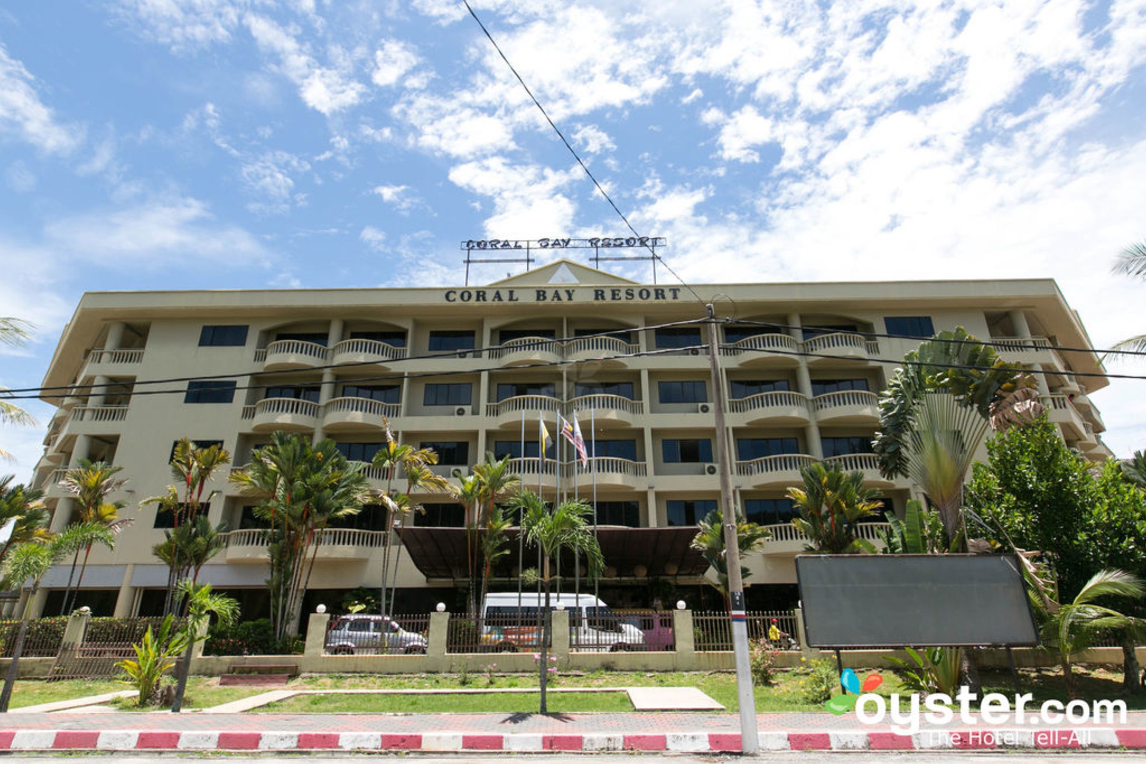 A multi-story hotel named Coral Bay Resort with balconies, palm trees, and a clear sky.