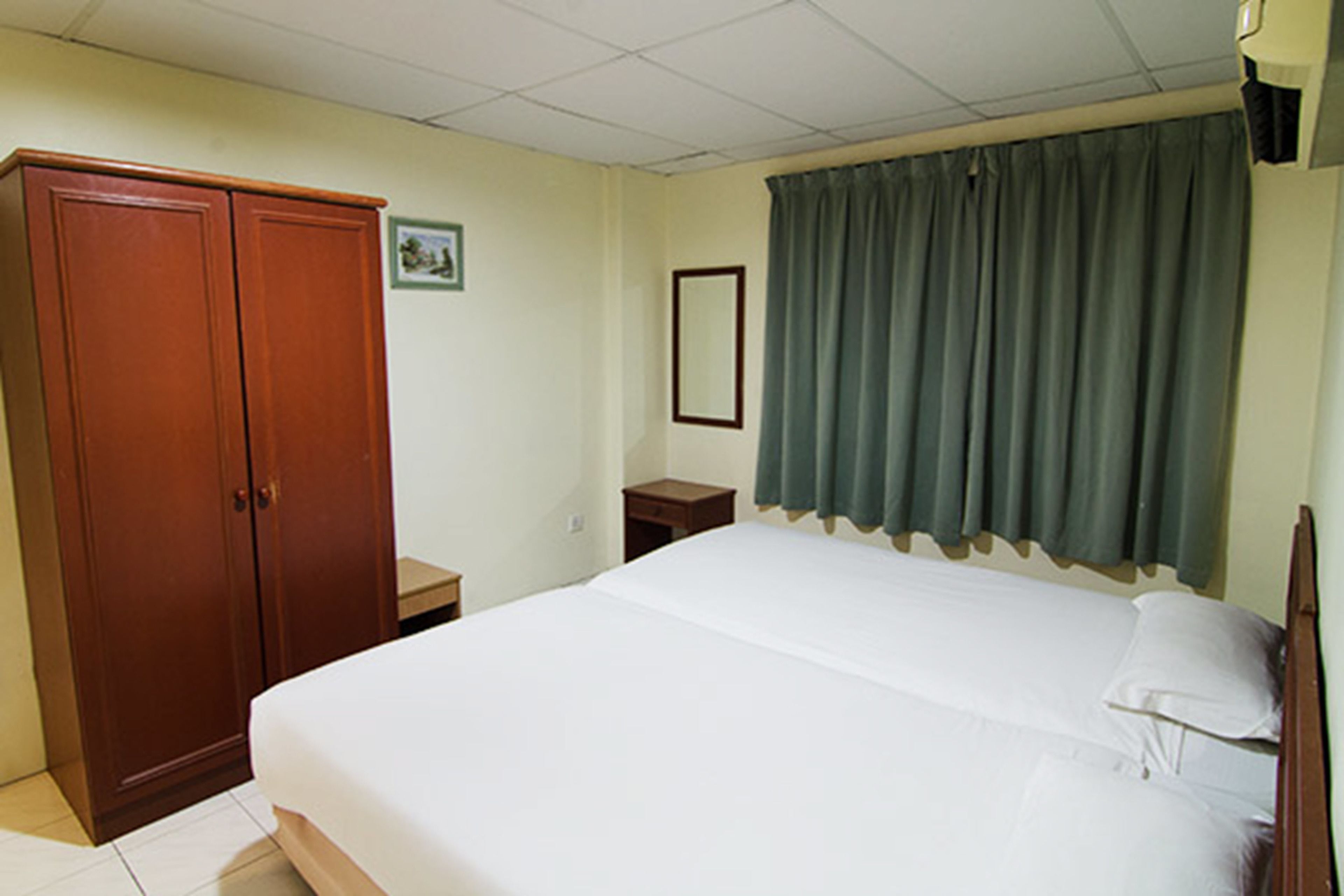 Un dormitorio con cama, armario, mesita de noche y ventana con cortinas.