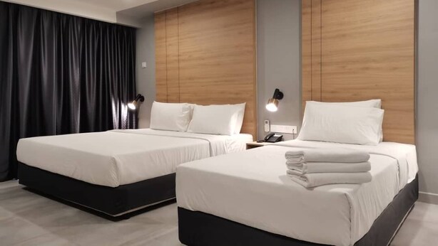 Ein modernes Hotelzimmer mit zwei Betten, dunklen Vorhängen, Holzkopfteilen, Nachttischlampen und einem Spiegel.