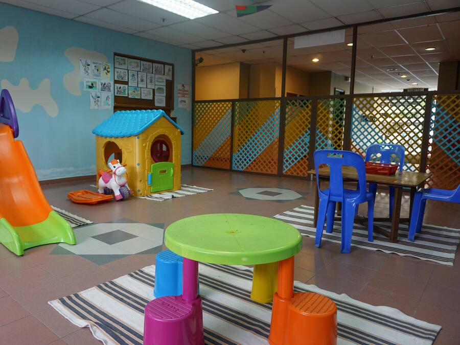 Ein Spielbereich für Kinder mit Rutsche, Spielhäuschen und bunten Hockern.